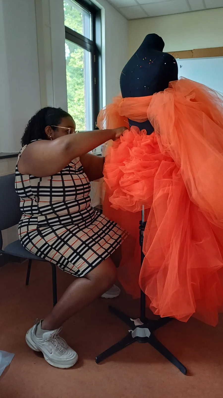 Dezelfde oranje rok van dichtbij: een hand zet de geplooide tule vast op de paspop.